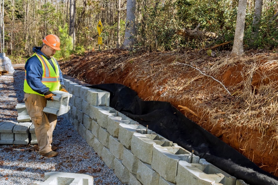 Builder placing concrete blocks against a cut earth bank during earthworks in Dapto