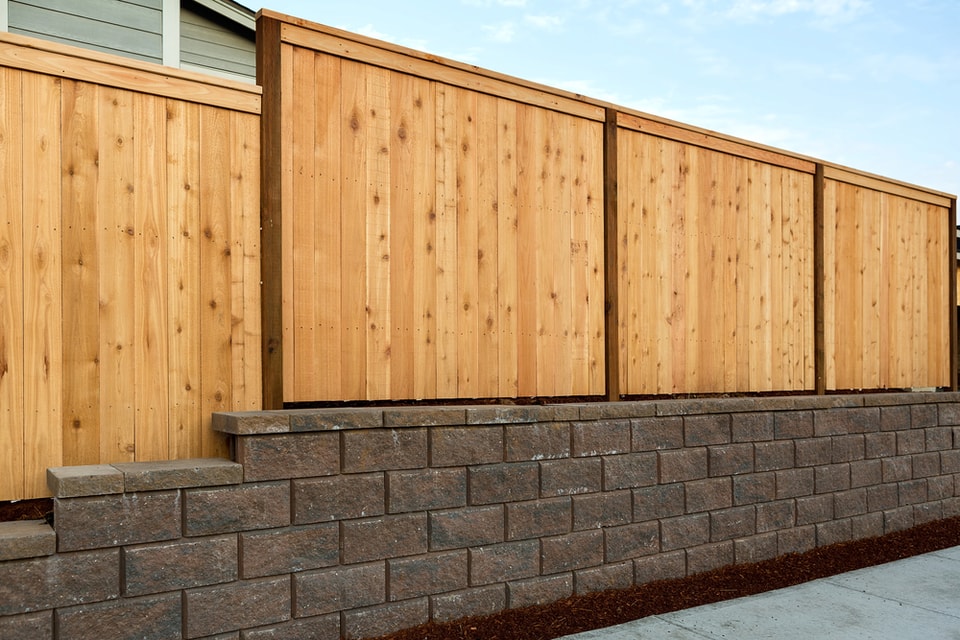 Brown block retaining wall supporting a timber fence in Thirroul