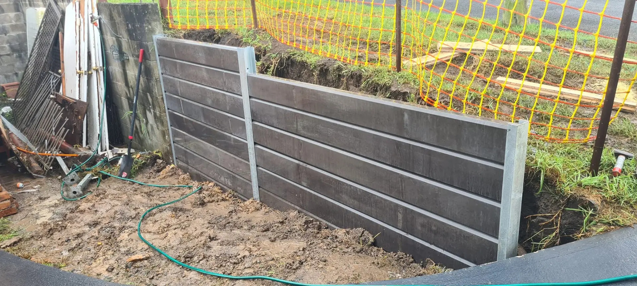 Charcoal concrete sleeper retaining wall being installed between galvanised steel posts
