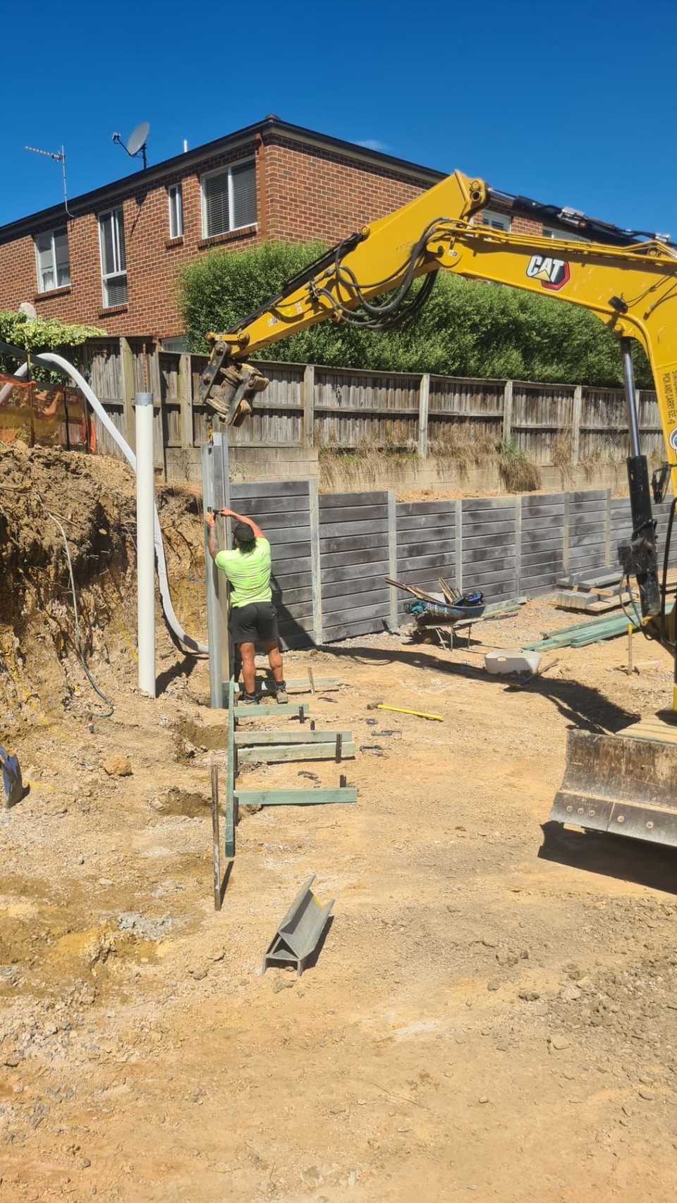 Concrete sleeper retaining wall being installed with steel posts and an excavator on a Kiama site