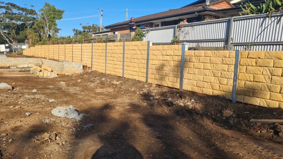 Sandstone-look concrete sleeper retaining wall with galvanised steel posts running along a Dapto boundary