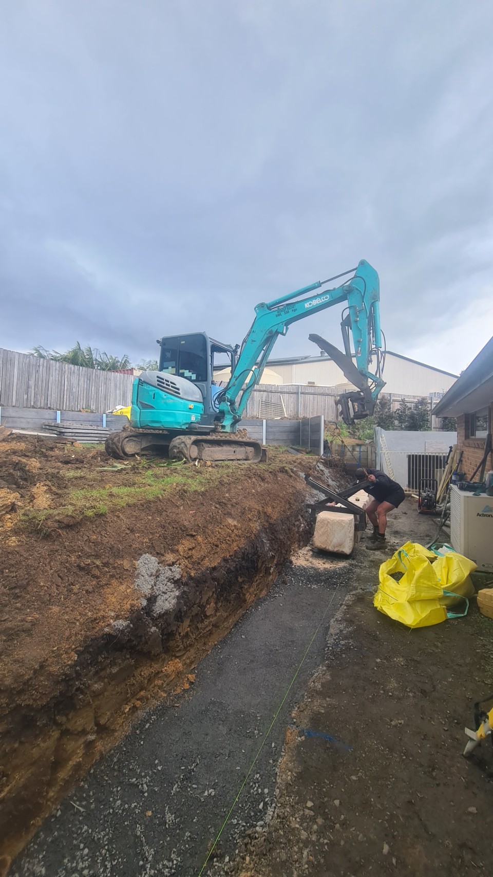 Mini excavator cutting a batter and trench during side-of-house earthworks in Thirroul
